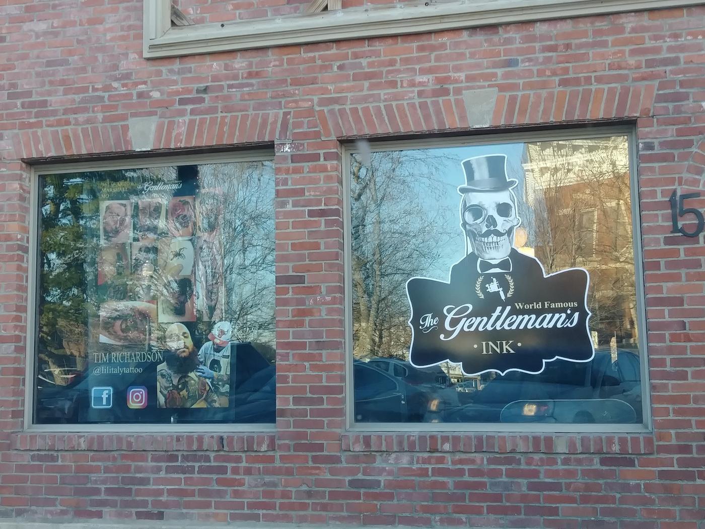 The two shop windows, one carrying the skull and top hat sign, the other a board of tattoo photographs