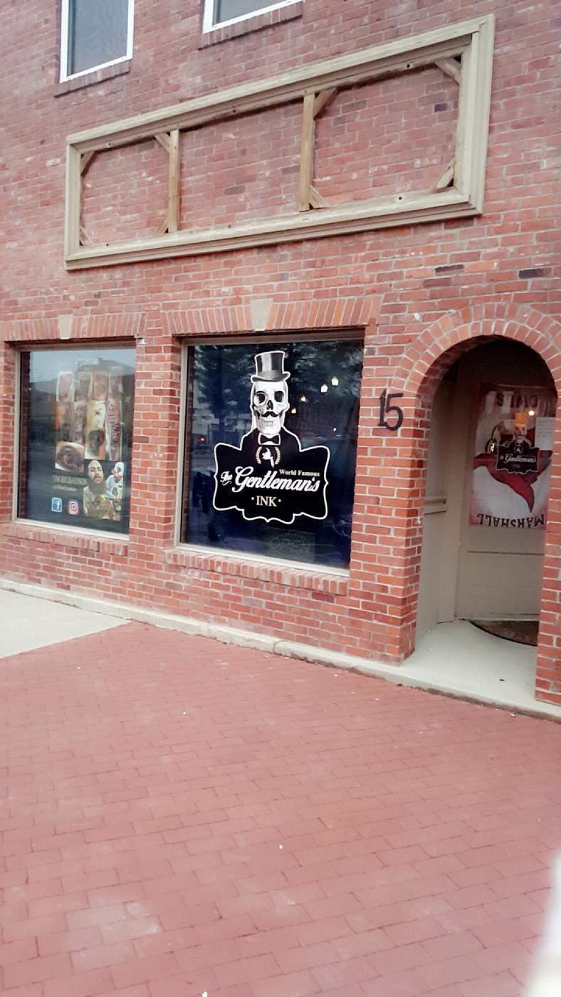 The Gentleman's Ink storefront at 15 N Lafayette Avenue, red brick with the skull and top hat painted on the window