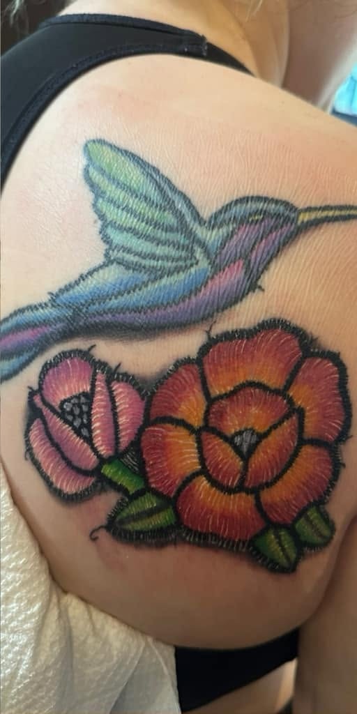Color hummingbird above two open flowers, on a shoulder