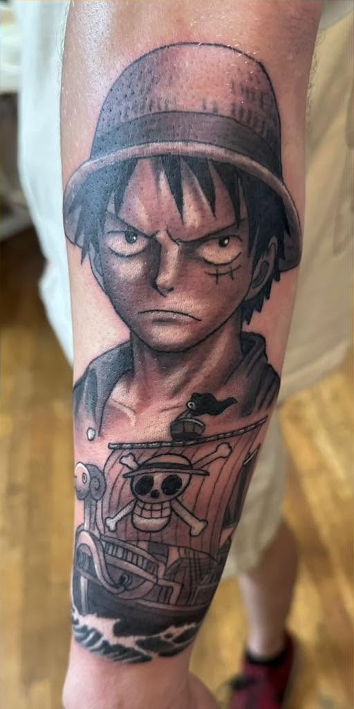 Anime character in a straw hat above a ship, on a forearm