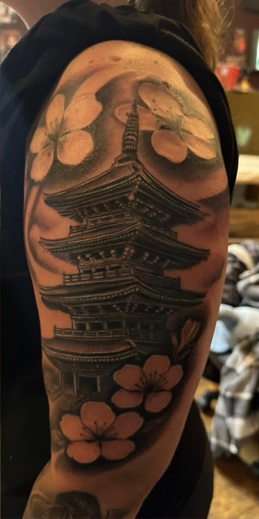 Black and gray pagoda framed by blossom, on a shoulder