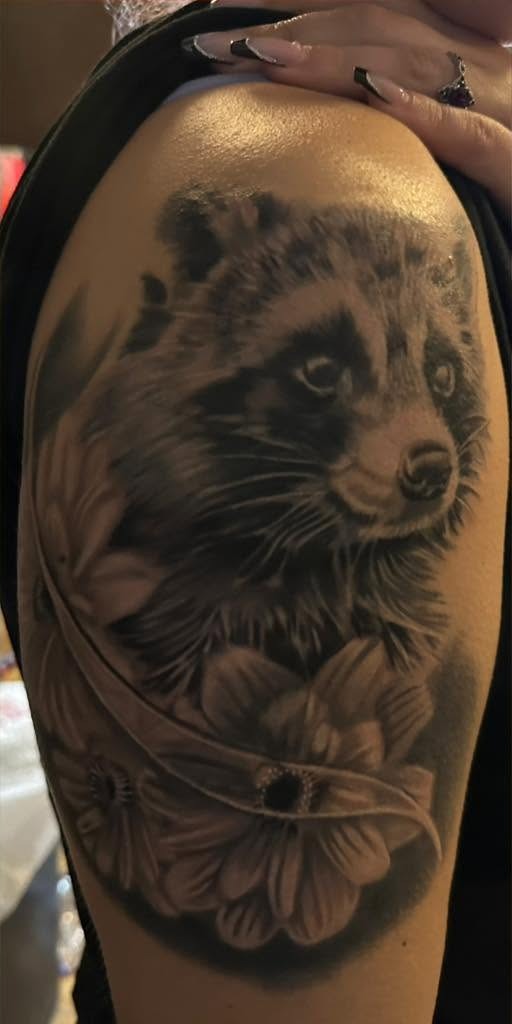Black and gray raccoon among flowers, on a shoulder