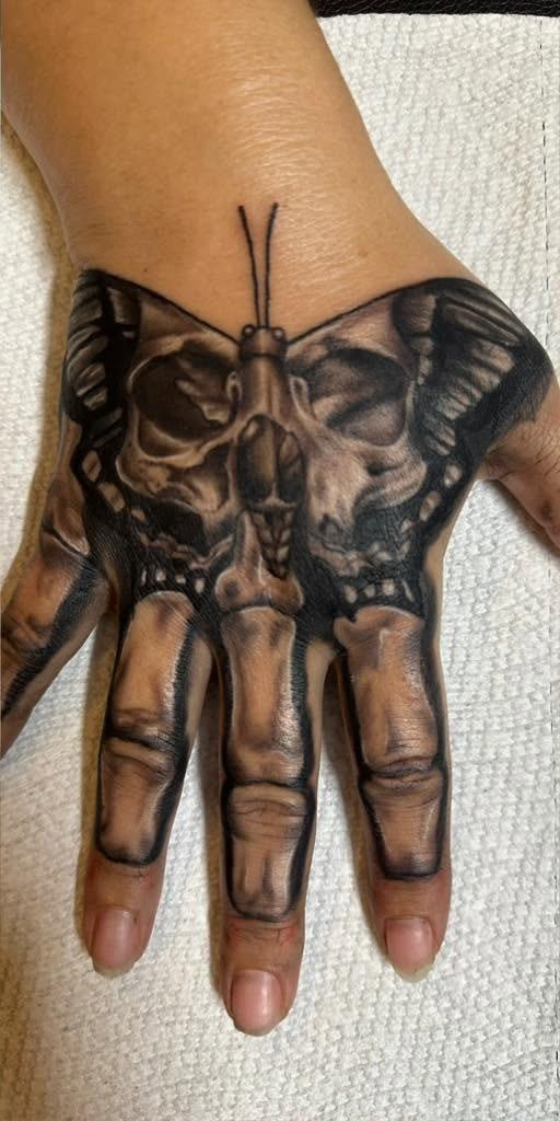 Black and gray moth with skulls in its wings, tattooed across the back of a hand