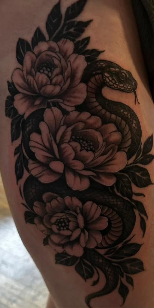Black and gray snake winding through open peonies, on an upper arm